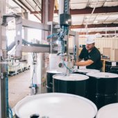 A man in a white hard hat handles drums of chemicals at a local Pelham industry.