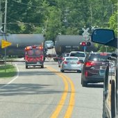 A train moves through a railroad crossing while an ambulance with lights flashing waits for the train to pass.