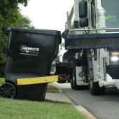 An Amwaste garbage truck picks up a garbage cart with a mechanical arm.