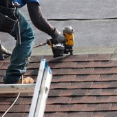 A roofer nails brown shingles to a roof.