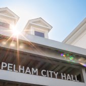 The exterior of Pelham City Hall with silver lettering spelling out Pelham City Hall and a sunbeam peeking over the roofline.