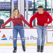 A happy couple wearing red shirts and jeans ice skates at the Pelham Civic Complex & Ice Arena.