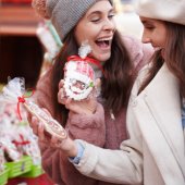 Two young women shop at a Christmas market. They're holding a Santa cookie wrapped in cellophane.