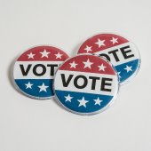 Three round lapel pins with the words "vote" on it.