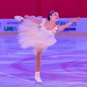 A young lady in a white figure skating costume glides over the ice at the Pelham Ice Arena.