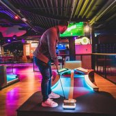 A man plays indoor carpet golf in a colorful, high-tech setting.