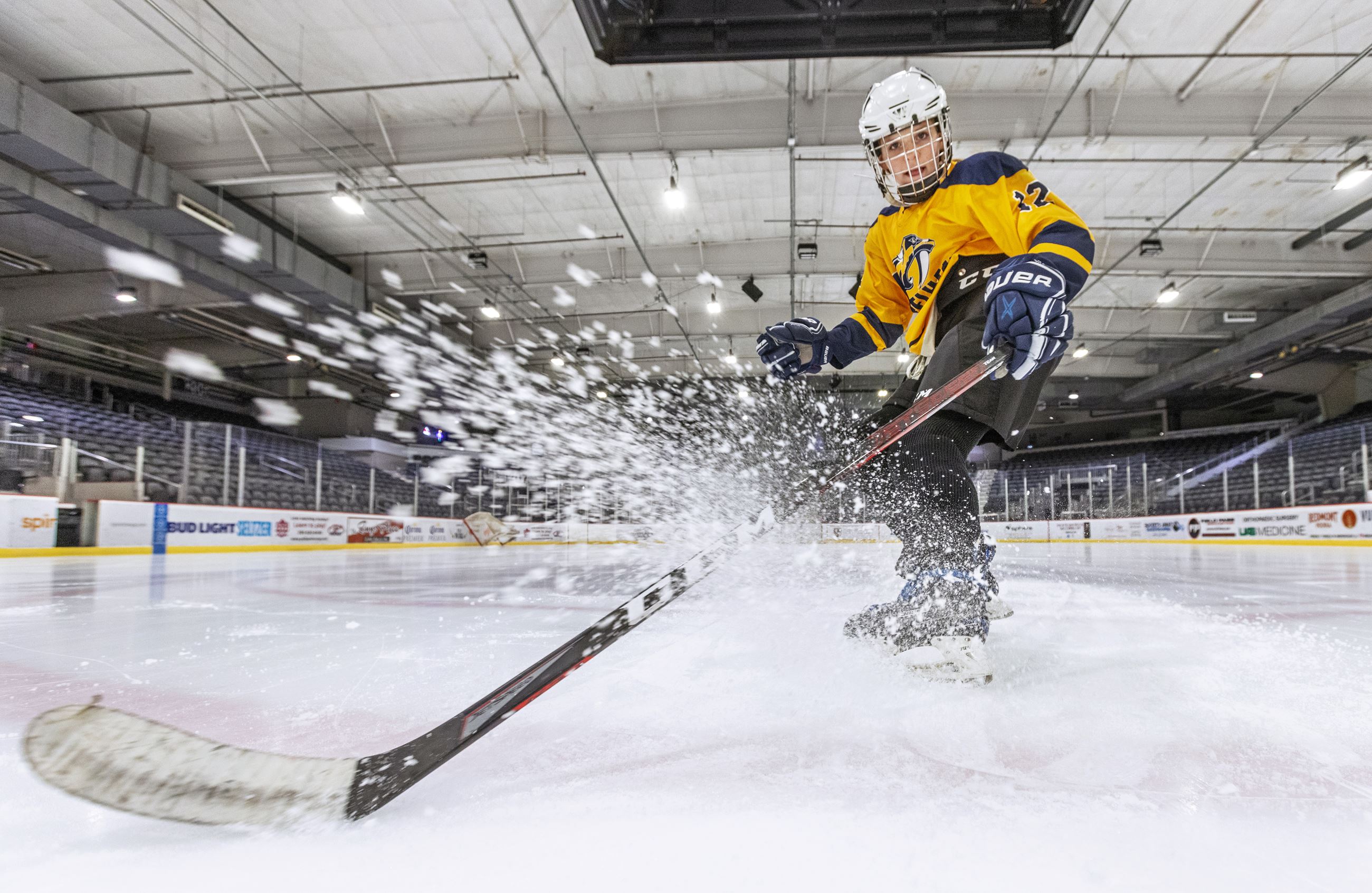 Youth hockey player skating on ice with hockey stick kicking up ice