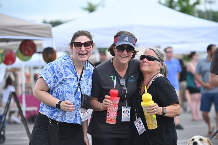 three women smiling at camera during community event outdoors