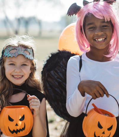 Two trick or treaters outside smiling with candy bucket